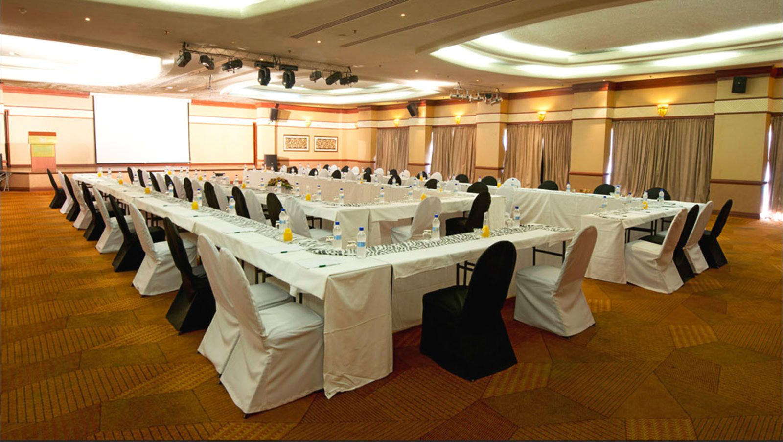 Conference hall from above, long rows of tables with notepads and water glasses facing a lectern